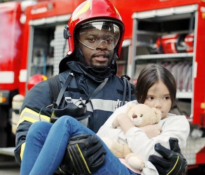 firefighter carrying child holding a teddy bear